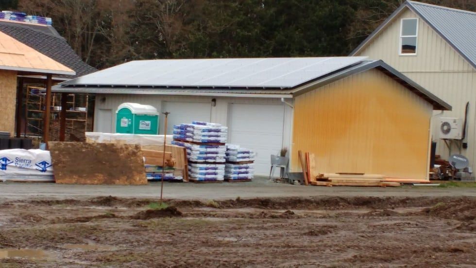 Construction site with a partially built garage, lumber, bags of material, and a porta-potty.