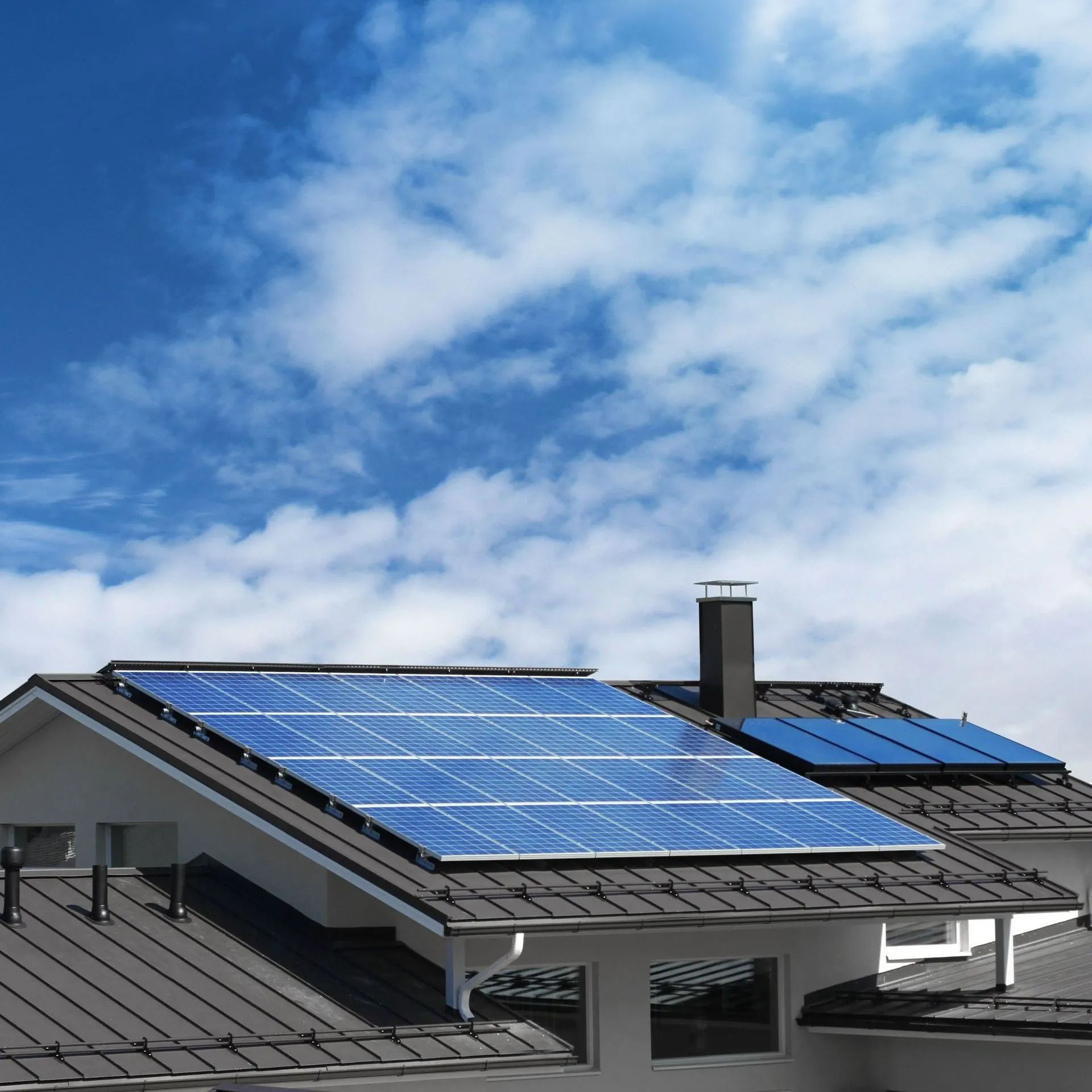 Solar panels on a residential roof against a blue sky with clouds.