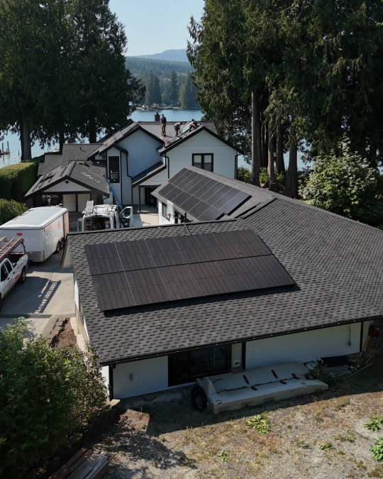 House with solar panels on the roof near a lake, trees in the background, a sunny day.