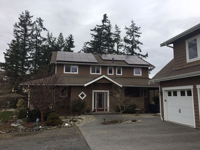 Two-story brown house with solar panels on the roof and a driveway leading to the front door.