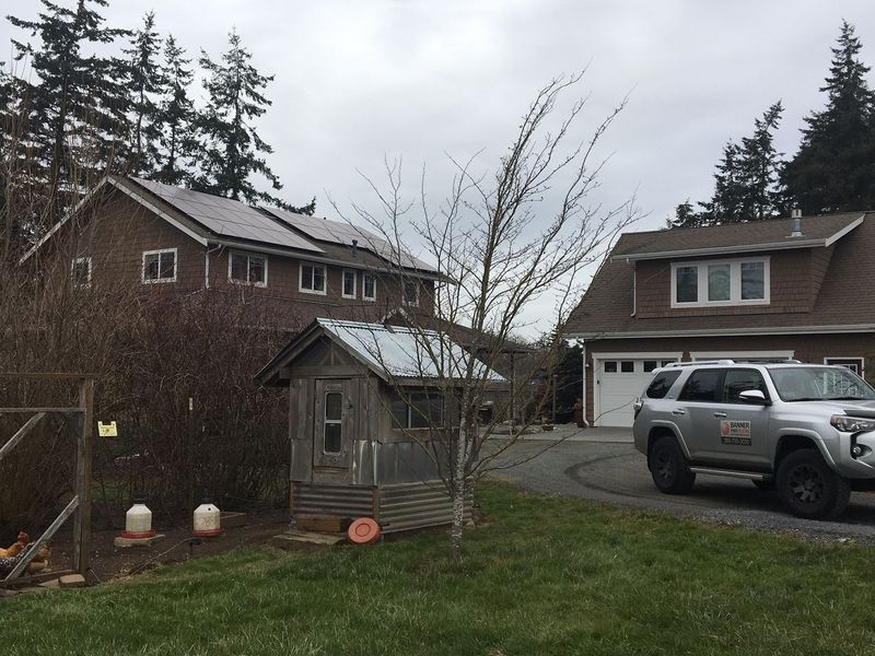 Two-story brown house with solar panels, a chicken coop, and a silver SUV parked in the driveway.