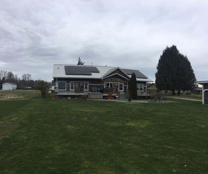 House with solar panels on roof, deck, and green lawn under cloudy sky.