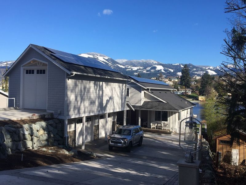 House with solar panels on roof, driveway, and mountain backdrop on a sunny day.