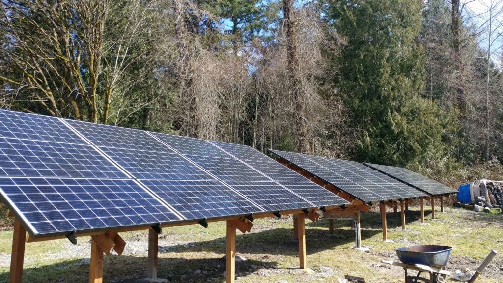 Solar panels on wooden supports in a grassy area with trees in the background.