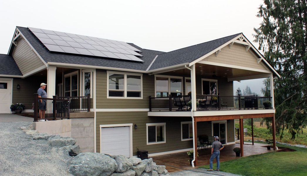 Two-story house with solar panels on the roof and a large deck. Two people are near the house.