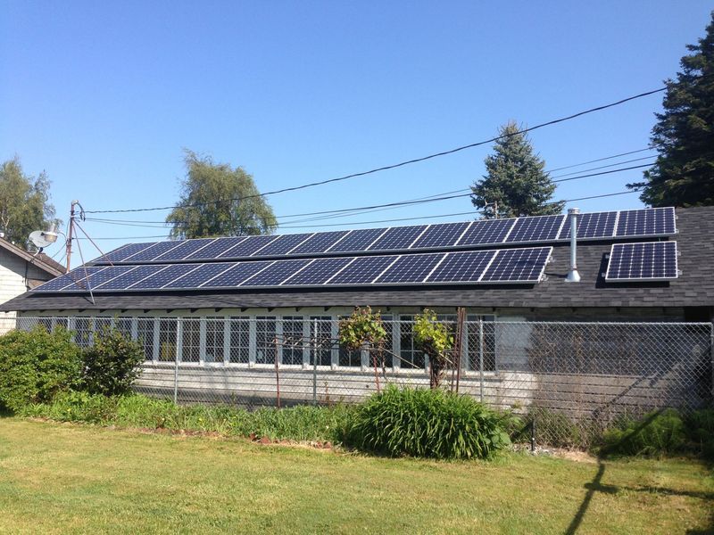 Solar panels on a building's roof with many windows, generating renewable energy under a clear blue sky.