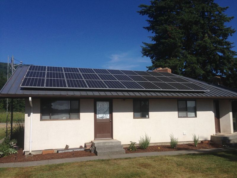 Solar panels on a residential roof, sunny day. Cream-colored house with a dark metal roof.