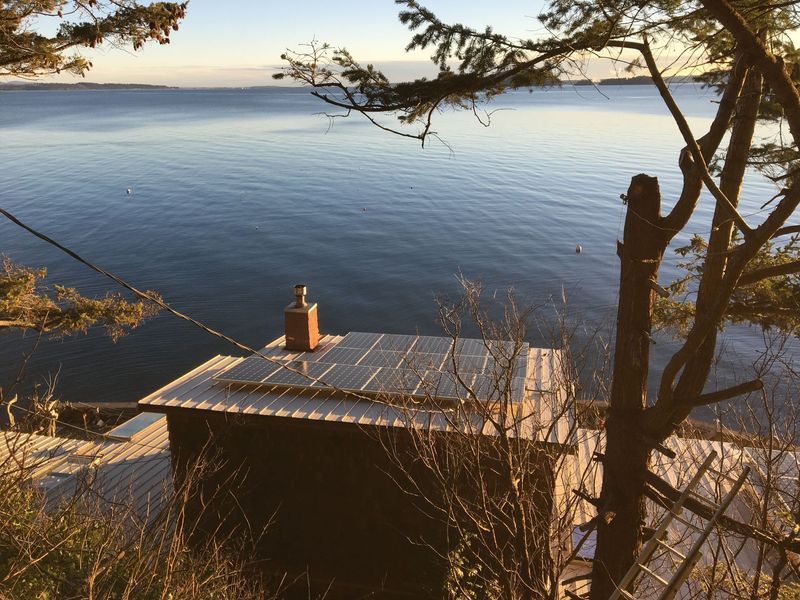 Small building with solar panels on roof, overlooking calm water at dawn.