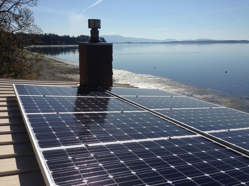 Solar panels on a rooftop with chimney, lake view in the background.