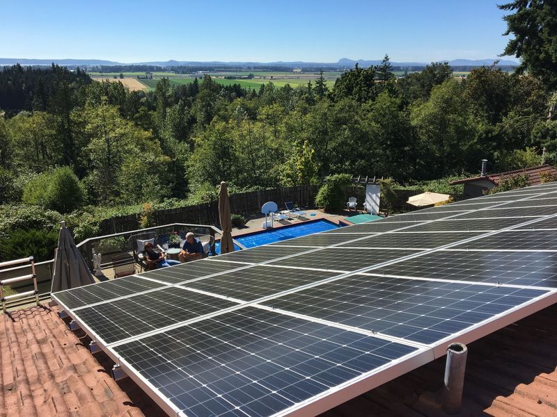 Solar panels on a rooftop overlook a pool and expansive green landscape. Blue sky.
