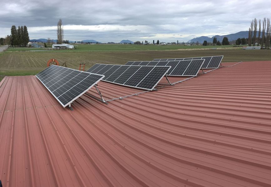 Solar panels on a red metal roof with a field and mountains in the background.