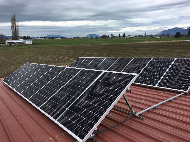 Solar panels on a red roof with farmland and mountains under an overcast sky.