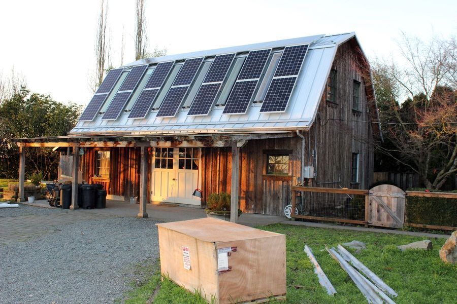 Barn with solar panels on the roof, wooden exterior, gravel driveway, and a wooden crate in front.