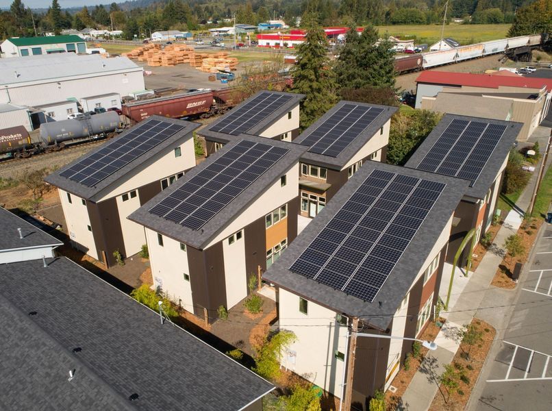 Solar panels on roofs of connected townhouses in a small town; train in background.