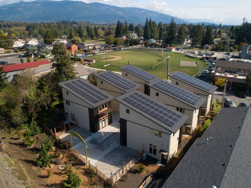 Solar panels on the roofs of multiple modern townhouses, green grass and mountains in the background.