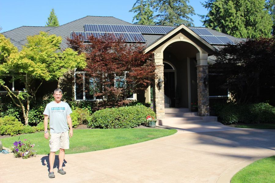 Man stands in front of a house with solar panels on the roof and a curved driveway.