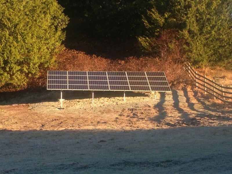 Solar panels mounted on a metal frame, set against a backdrop of trees, with a frosted foreground and a wooden fence.