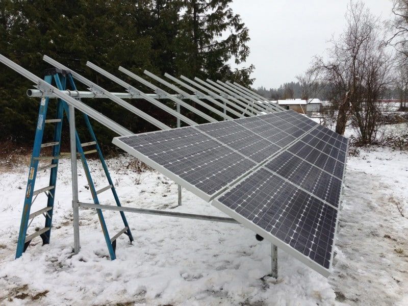 Solar panels installed outdoors on a snowy day, with a ladder leaned against the frame.