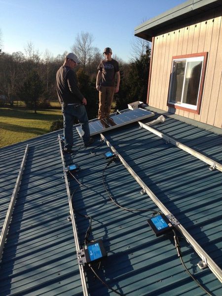 Two people installing solar panels on a metal roof. Blue panels, sunny day.