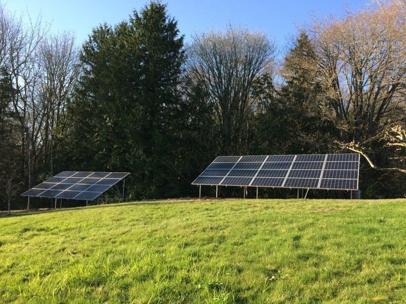 Two solar panel arrays on a grassy field with trees in the background under a blue sky.