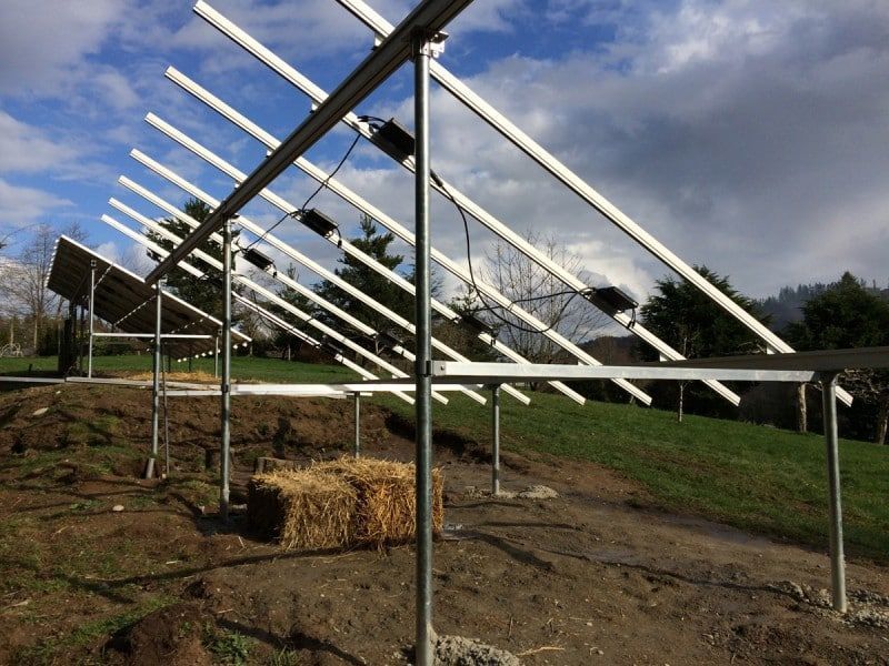 Solar panel mounting system under construction on a grassy hillside, with metal frames angled towards the sky.