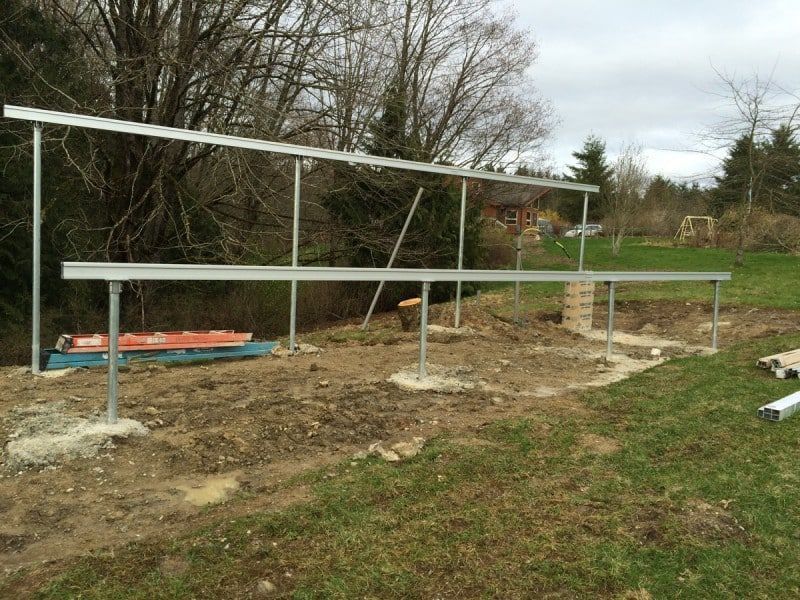 Steel frame for solar panels being built outdoors on a grassy plot.