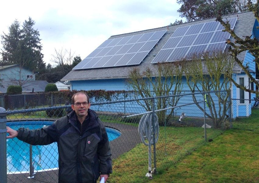 Man standing next to a pool in front of a blue house with solar panels on the roof.