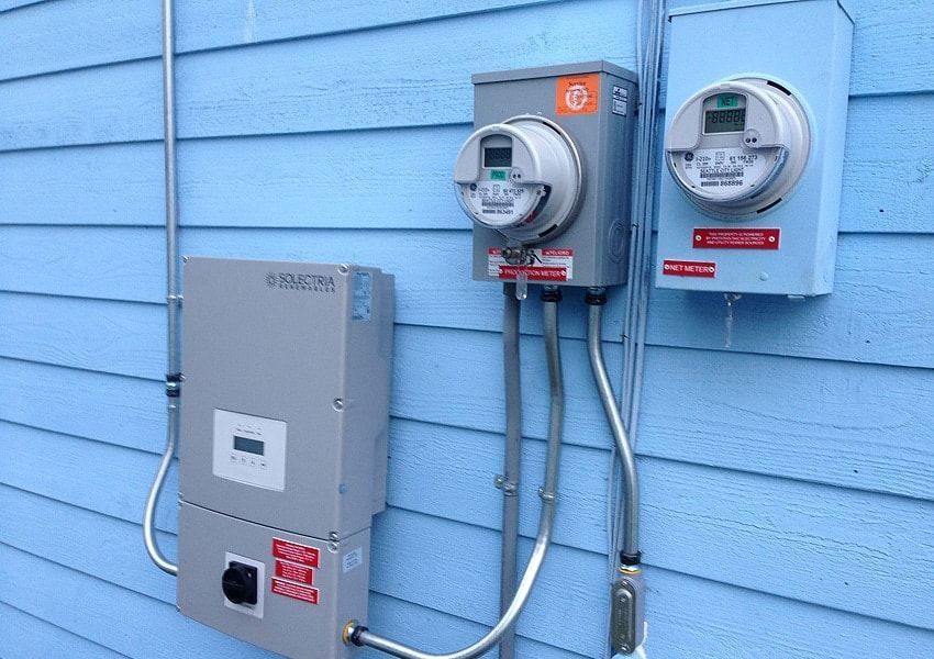 Electrical meters and inverter box mounted on blue siding.