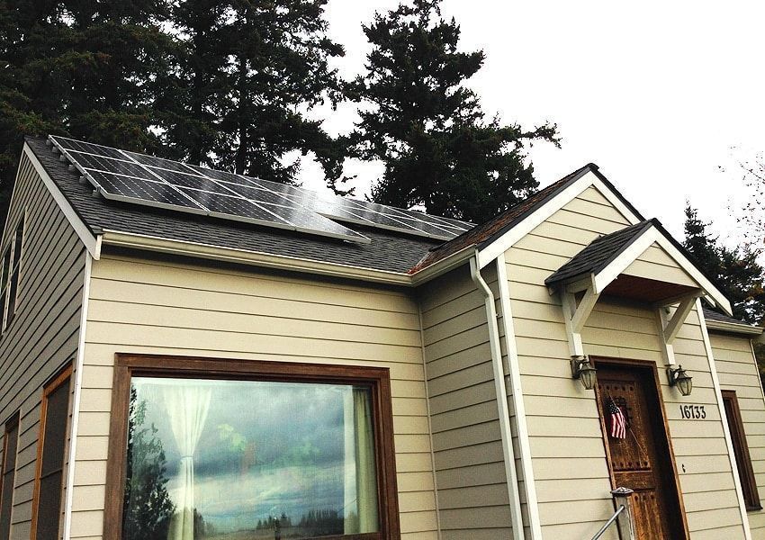 Solar panels on a beige house roof, with dark green trees in the background.