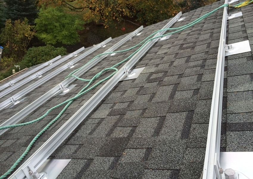 Solar panel mounting hardware on a shingled roof, with green electrical wiring.