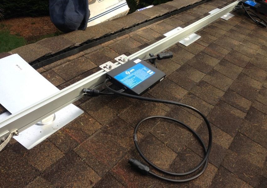 Solar panel mounting hardware on a shingled roof, showing a power optimizer connected to a rail.