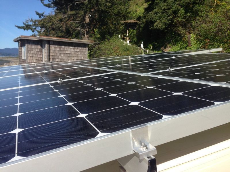 Solar panels installed on a roof with a small wooden structure nearby.