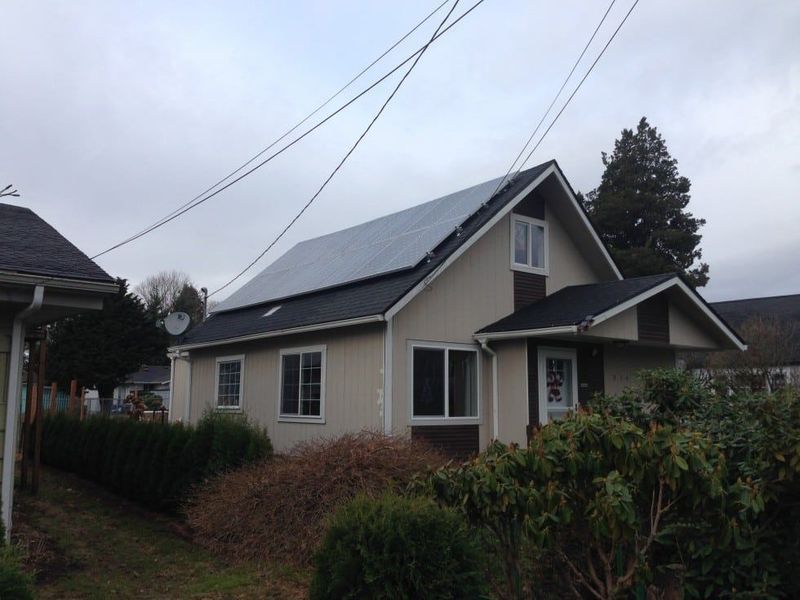 Beige house with solar panels on the roof, under a cloudy sky.