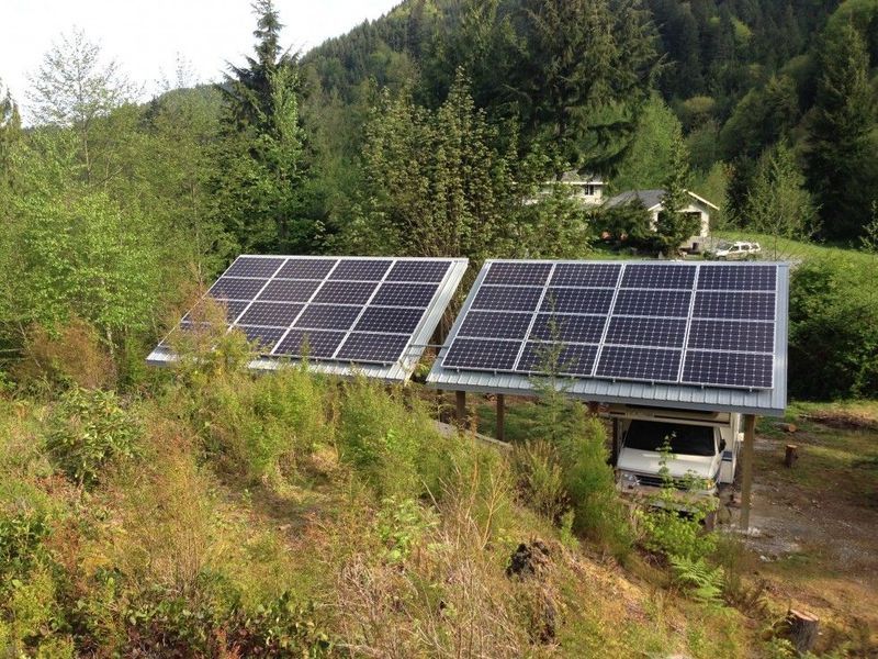 Two solar panel arrays over a carport on a hillside, surrounded by vegetation and trees.