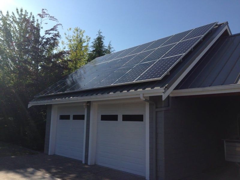 Solar panels on the gray roof of a two-car garage with white doors, under a blue sky.