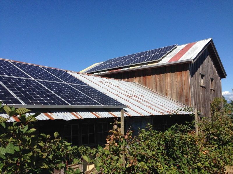 Solar panels installed on the weathered roof of a rustic barn against a clear blue sky.