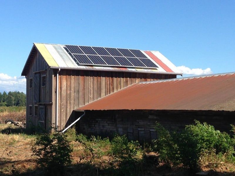 Solar panels on the roof of an old, weathered barn under a blue sky.