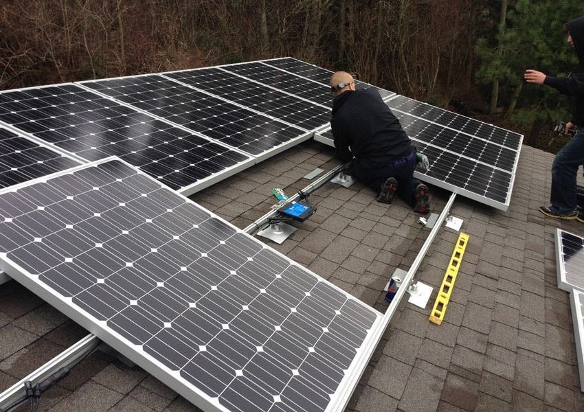 Solar panel installation on a rooftop with workers adjusting panels, using a level.