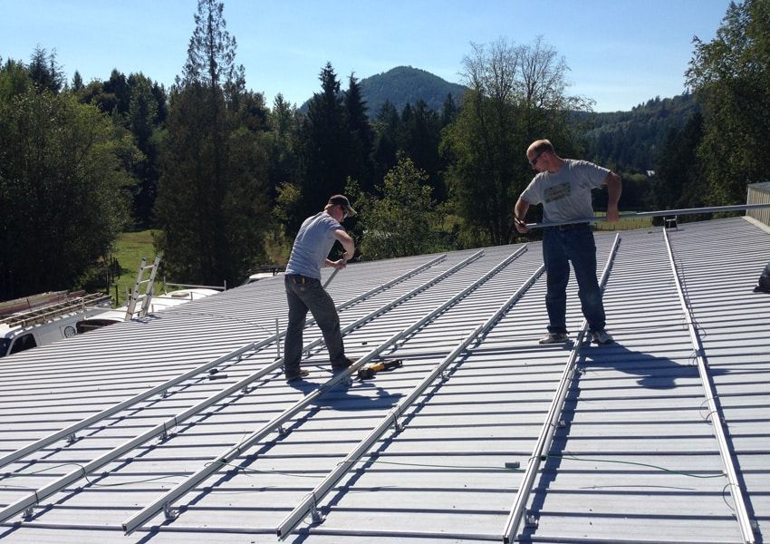 Two people installing solar panel rails on a rooftop on a sunny day.