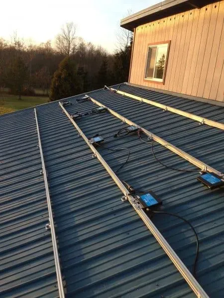 Solar panel mounting system on a corrugated metal roof; blue-green roof with silver rails and black boxes.