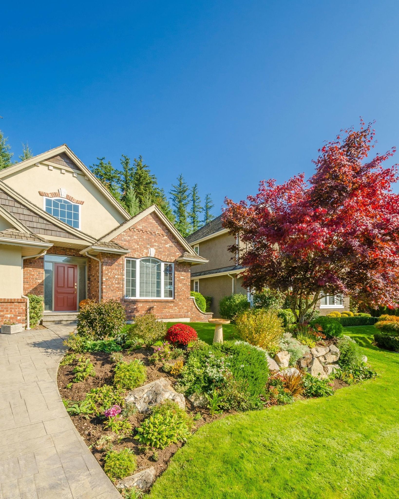 A brick house with a lush green lawn and a tree in front of it.