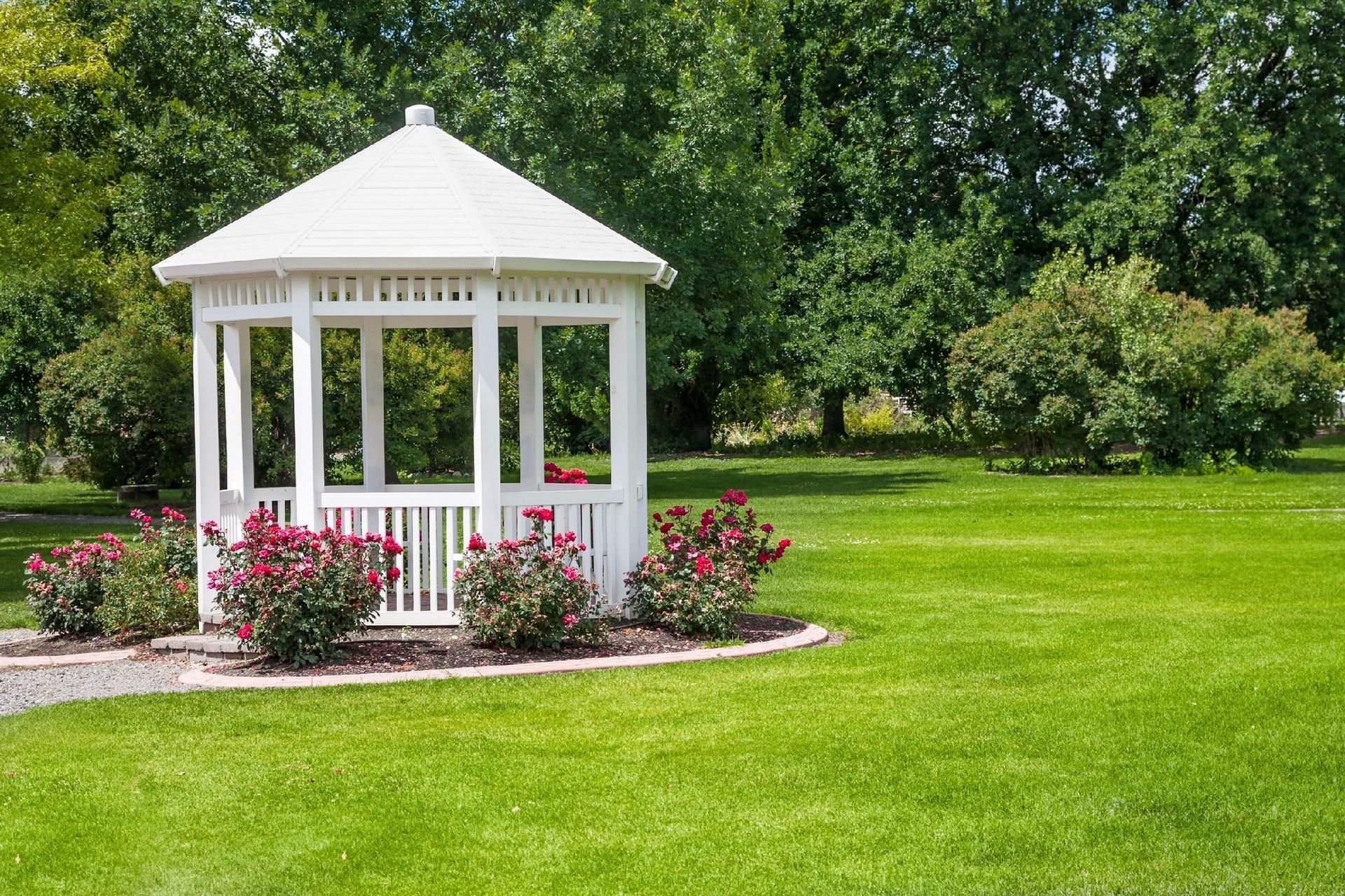 A white gazebo is sitting in the middle of a lush green field.