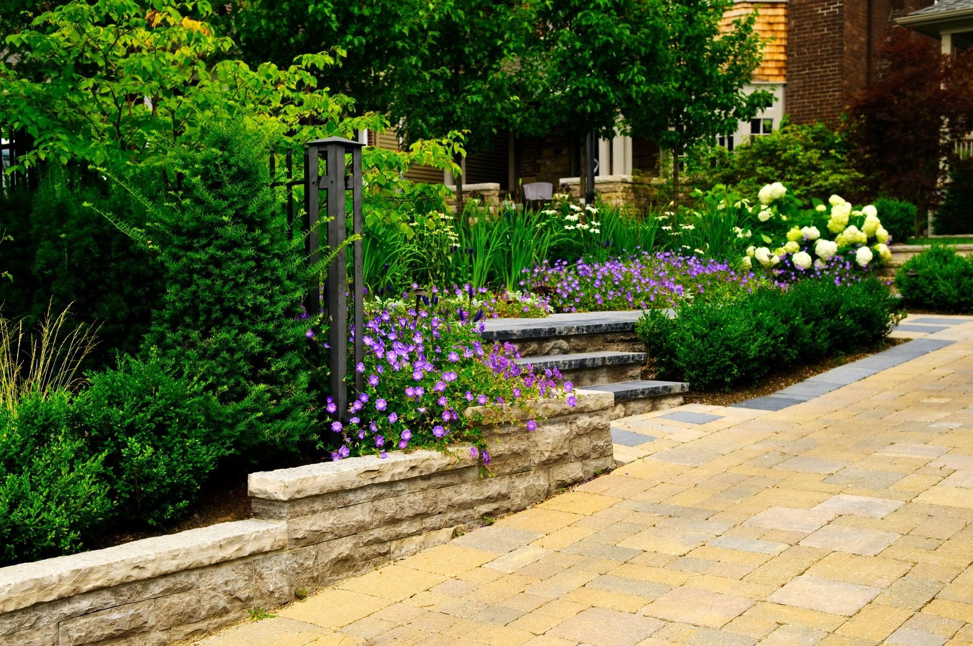 A brick walkway leading to a garden with purple and white flowers.