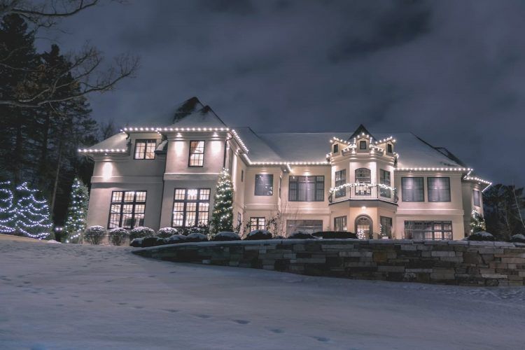 A large house with christmas lights on it is covered in snow.
