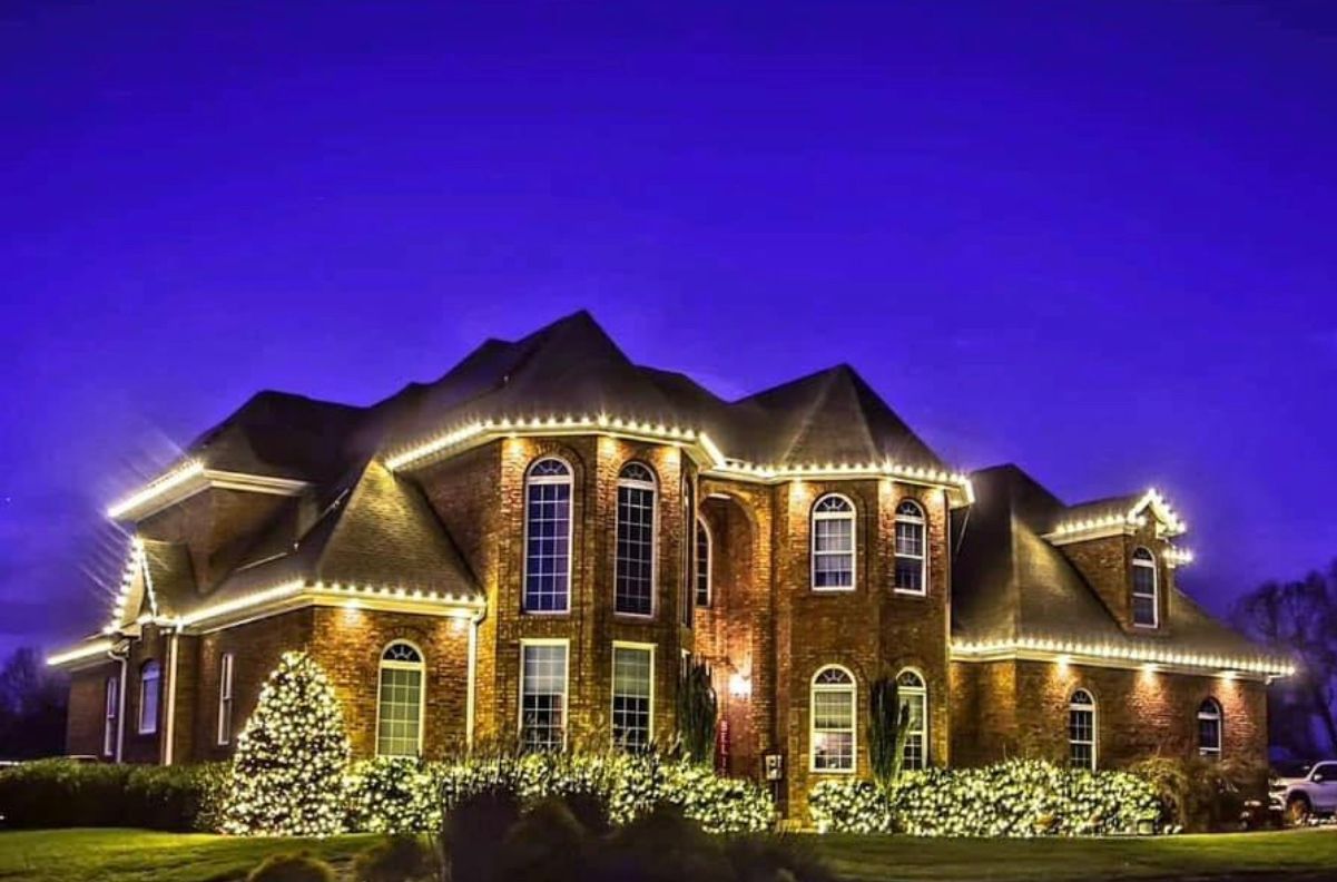 A large brick house is decorated with christmas lights at night.