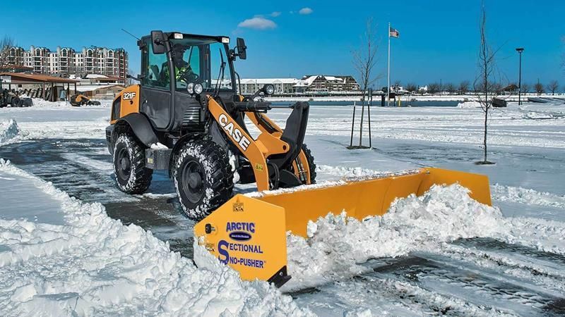A snow plow is clearing snow from a parking lot.