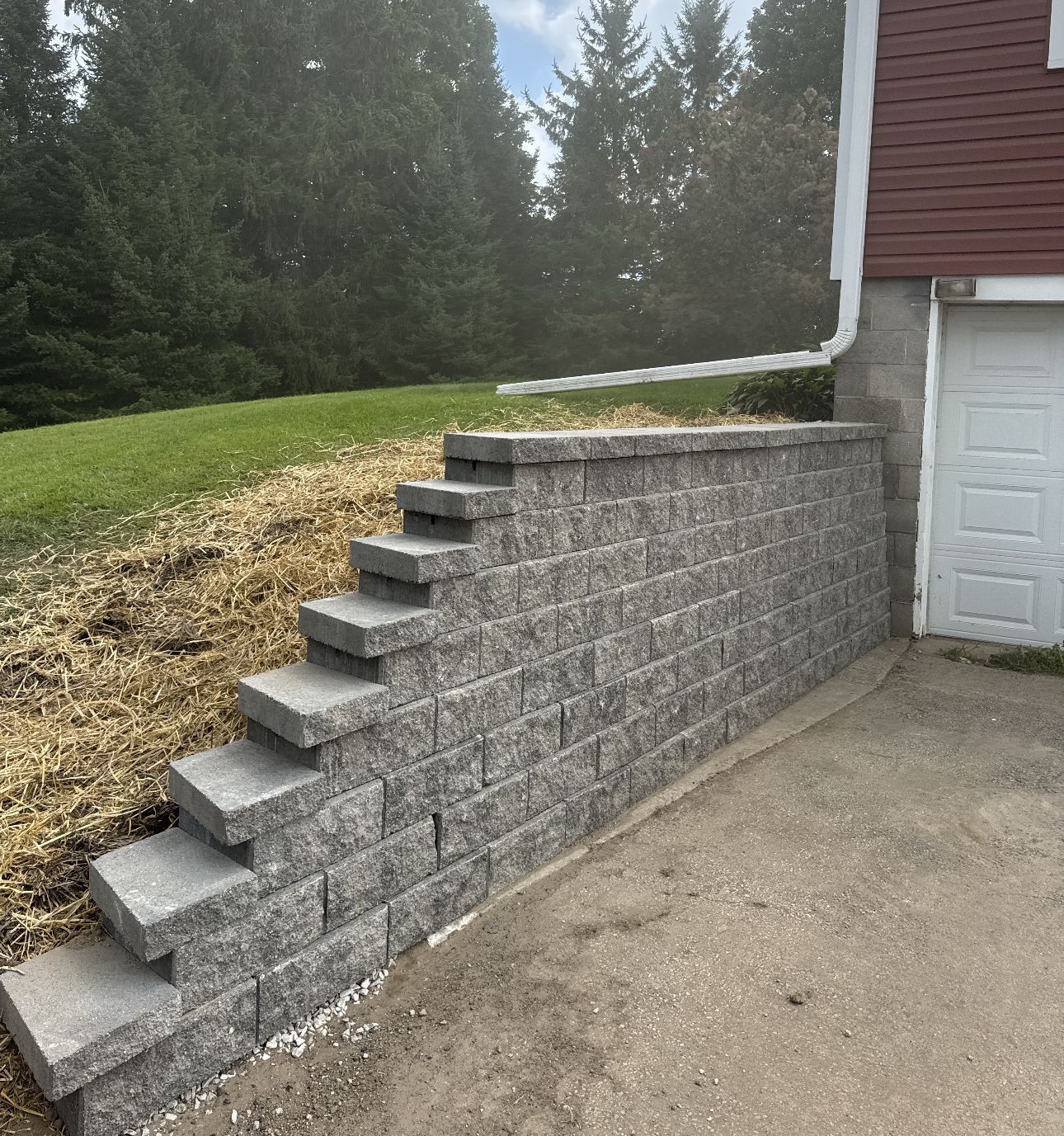 Gray block retaining wall with steps leading up to a grassy area, next to a garage.