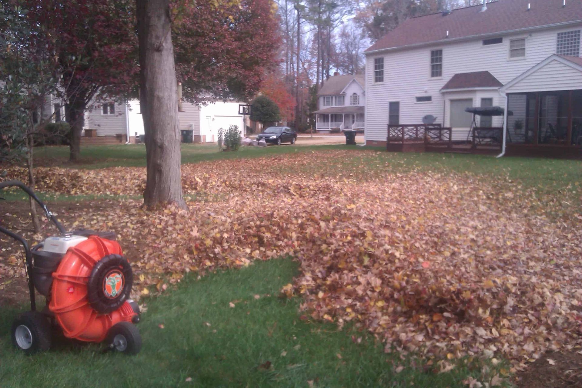 A lawn blower is sitting on the grass near a pile of leaves
