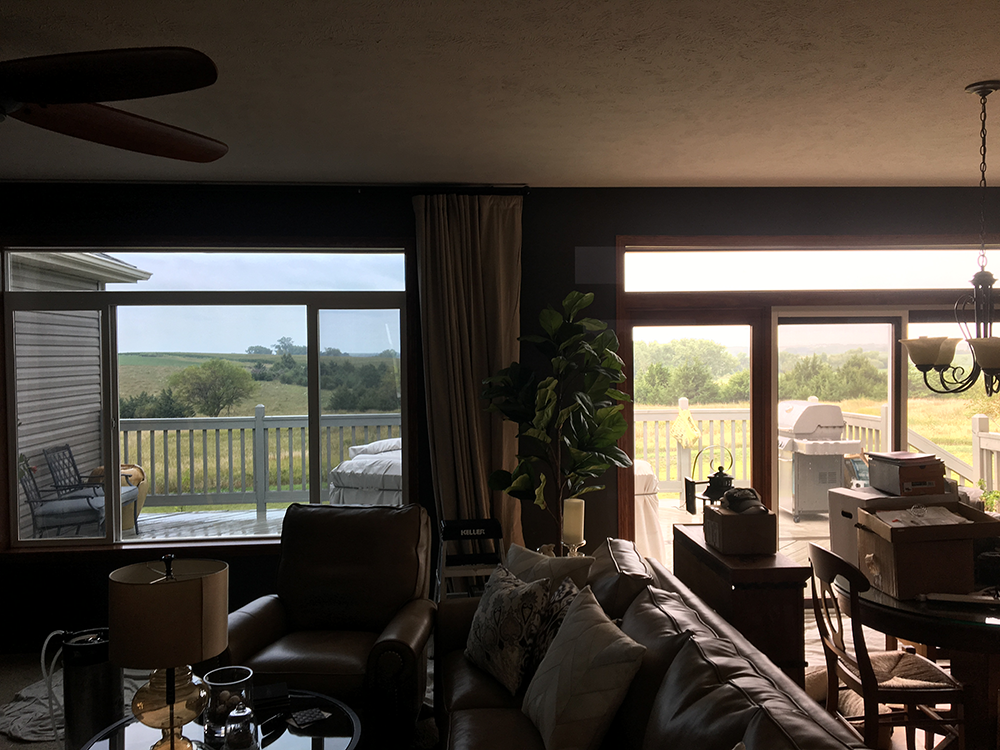 Sunlit living room with dark furniture, large windows, balcony view, and dining table by the window