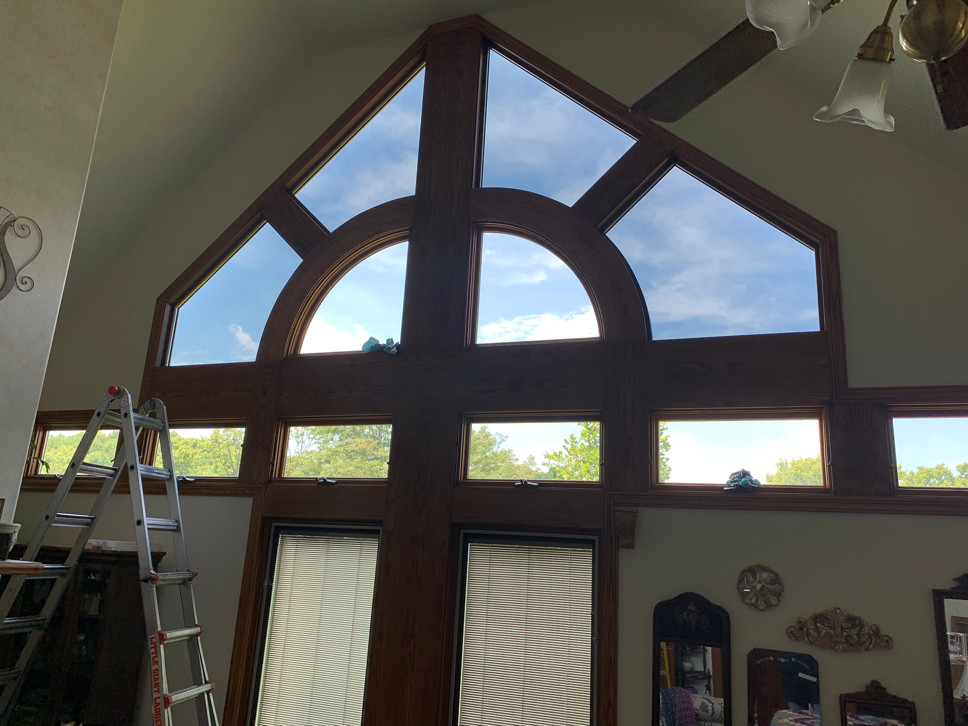 Tall indoor window wall with a large circular center and triangular panes above a ladder and door below